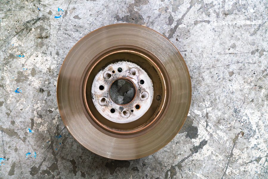 A worn brake rotor removed from a vehicle, showing scoring and heat discoloration