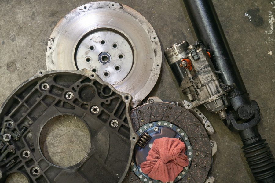 Flywheel, clutch disc, bellhousing, starter and driveshaft laid out on the shop floor