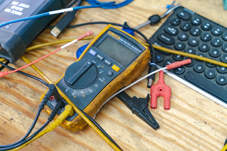 A Fluke 115 true RMS multimeter with test leads on a workbench