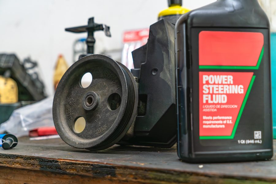 A power steering pump on the workbench beside a bottle of power steering fluid